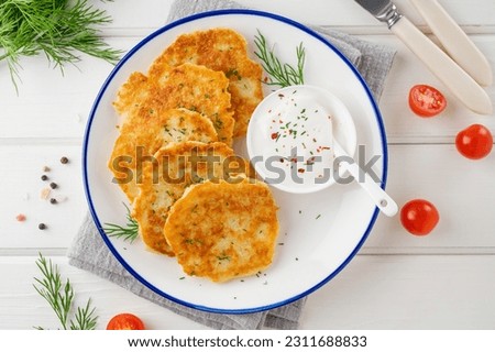 Potato pancakes, latkes or draniki with fresh herbs and sour cream on a plate on a white wooden background. Top view, copy space Royalty-Free Stock Photo #2311688833