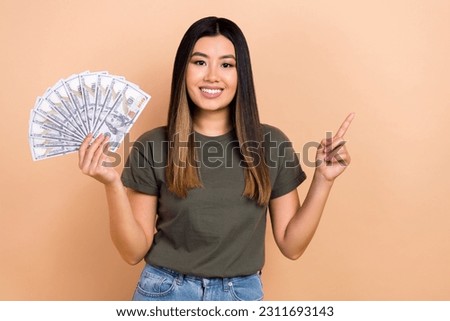 Photo of attractive nice person beaming smile hold dollar bills direct finger empty space isolated on beige color background