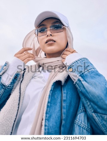 Portrait, fashion or low angle with a muslim woman outdoor in a cap, sunglasses and scarf for contemporary style. Islam, faith or hijab with a trendy young arab person posing alone in modern eyewear Royalty-Free Stock Photo #2311694703