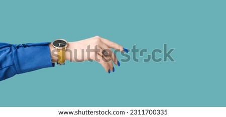 Female hand with golden wristwatch on blue background with space for text Royalty-Free Stock Photo #2311700335