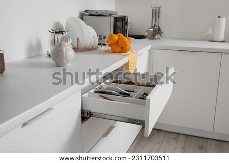 Open drawers with utensils in light kitchen Royalty-Free Stock Photo #2311703511