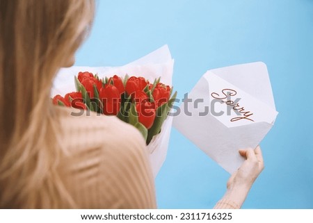 Apology. Woman holding Sorry greeting card and bouquet of tulips on light blue background, closeup