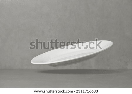 Empty white plate falling on the table. Levitation, flying saucer. Royalty-Free Stock Photo #2311716633