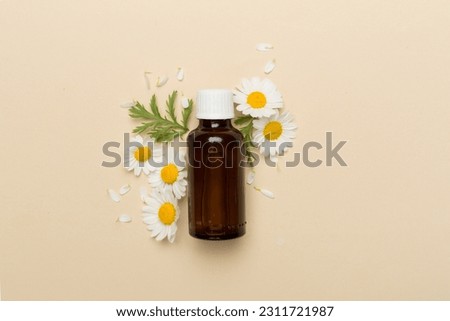 Bottle with chamomile essential oil and flowers on color background, top view
