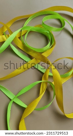 Green and yellow ribbons made of cloth are placed randomly on a beige mat. 