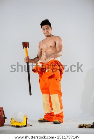 Attractive topless firefighter is standing and holding an iron axe in one hand while giving a thumbs up with the other hand on a white background.