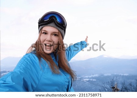 Smiling woman with ski goggles taking selfie in snowy mountains