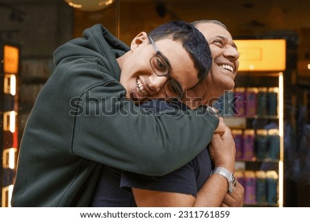 Heartwarming Connection: Smiling Boy Embracing Grandfather Amidst the Bustle of a Shopping Center. Royalty-Free Stock Photo #2311761859