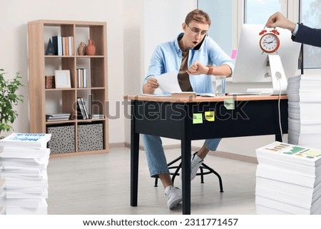 Deadline concept. Boss holding alarm clock near overwhelmed worker at desk in office
