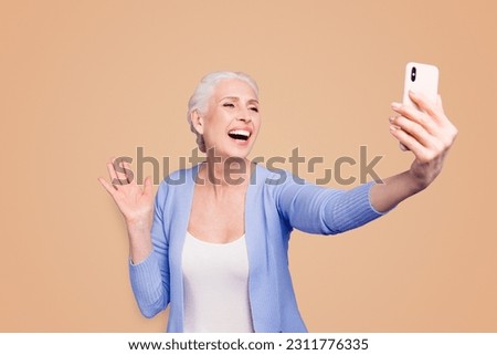 Grey haired old happy excited funny funky woman wearing casual, taking self picture, waving to cam, opened mouth. Isolated over violet purple background