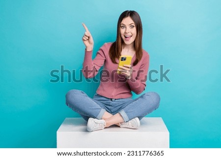 Full length photo of excited woman trendy shirt directing at eshop hold smartphone sit on platform isolated on teal color background