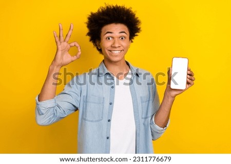 Photo of excited confident man wear jeans shirt showing okey gadget screen empty space isolated yellow color background