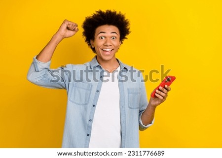 Photo of funky lucky guy dressed denim shirt rising fist texting apple iphone isolated yellow color background