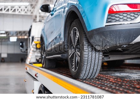 A broken-down vehicle is being hauled onto a flatbed tow truck with a cable for repair at a workshop garage. Royalty-Free Stock Photo #2311781087