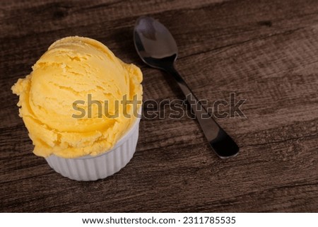 Vanilla ice cream served in a white bowl next to a spoon. Gourmet photograph of frozen desserts with empty space to the right of the image.