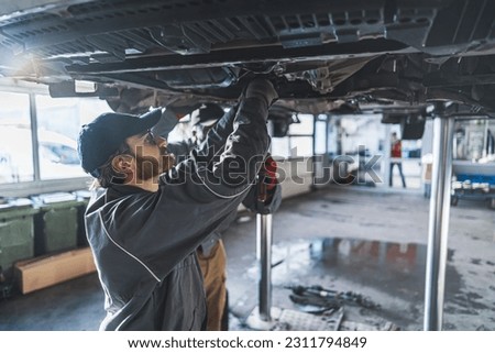 Men auto mechanics repairing car chassis raised on a lift inside service shop. High quality photo Royalty-Free Stock Photo #2311794849