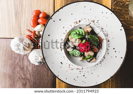 Top-down view of black tagliolini pasta dish with dried tomatoes and shrimp served on white plate on wooden table decorated with spices. Italian cuisine. Horizontal indoor shot. High quality photo