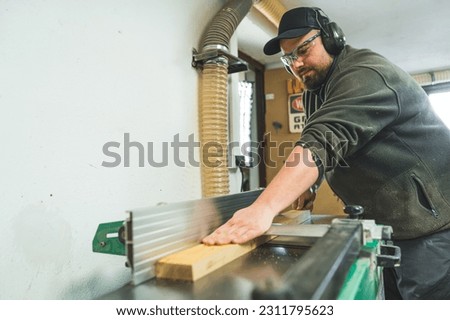 Medium shot of a carpenter using a table saw to cut a plank of wood while working in his woodworking studio. High quality photo Royalty-Free Stock Photo #2311795623