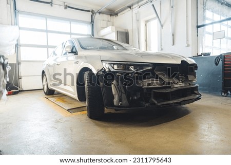 Automobile with front end damage inside a car body repair shop. High quality photo Royalty-Free Stock Photo #2311795643
