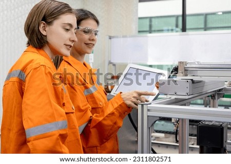Engineer caucasian woman testing an Artificial Intelligent robotic automatic arm machine in modern factory for transport parcel or container. Automation manufacturing for transportation industry.