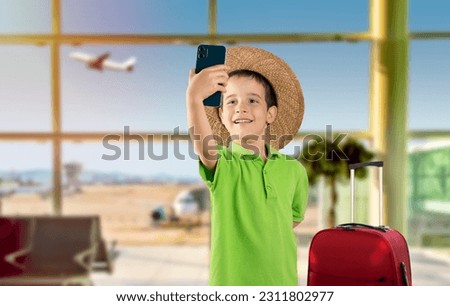 Caucasian little boy with hat and smiling making selfie by the smartphone at international airport.