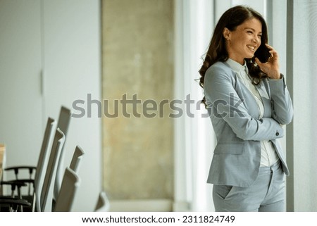 Pretty young woman using mobile phone by the office window