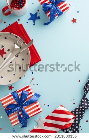Celebrate Fourth of July with this patriotic table arrangement. Vertical top view, featuring plate, cup, cutlery, napkin, confetti, tie, gift boxes on light blue background. Space for your text or ad