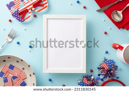 Add touch of patriotism to your table with Independence Day setup. Top view plate, mug, cutlery, napkin, sprinkles, headband, glasses, USA flags, light blue backdrop. Empty photo frame for picture