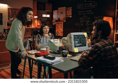 Group of young people working over new project at table with computers in garage Royalty-Free Stock Photo #2311831505