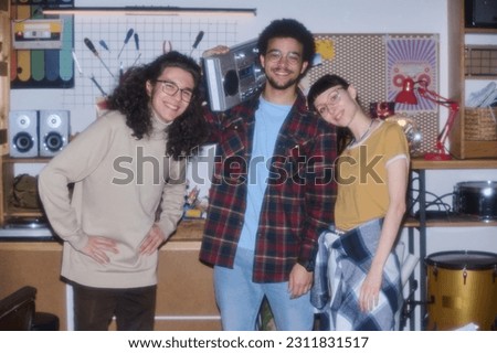Portrait of teenagers smiling at camera and listening to music on tape recorder standing in garage