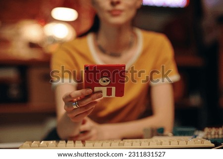 Close-up of young woman saving information on floppy disk while working on computer Royalty-Free Stock Photo #2311831527