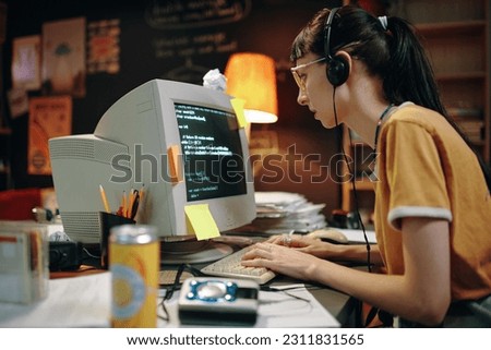 Young woman in headphones typing codes for new software on computer, she working at her workplace in garage Royalty-Free Stock Photo #2311831565