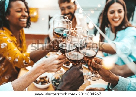People clinking red wine glasses on rooftop dinner party - Happy friends eating meat and drinking wineglass at restaurant patio - Food and beverage lifestyle concept with guys and girls dining outdoor