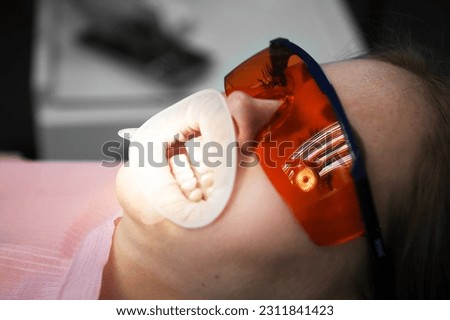 Woman wearing protective glasses getting teeth filling in a dental clinic. Disposable rubber mouth opener.  Royalty-Free Stock Photo #2311841423
