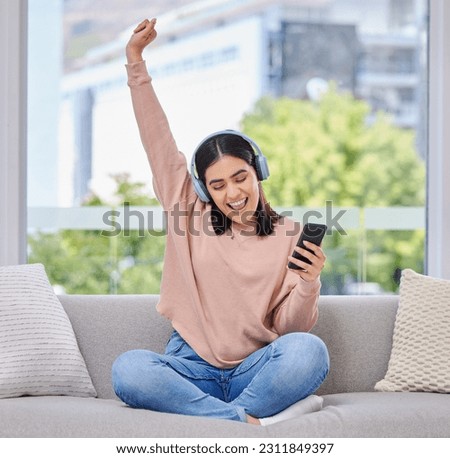 Woman, excited and phone with headphones for music on a home sofa with happiness and energy. Happy female person on a lounge couch with a smartphone for streaming or listen to audio, podcast or radio