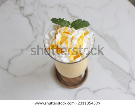 A glass of mango juicy with white cream on table.