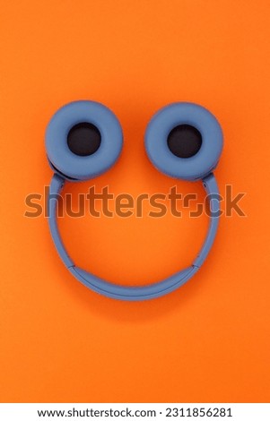 Face made of blue headphones on orange background. Wireless headphones. Headphones in the shape of a smile. Top view