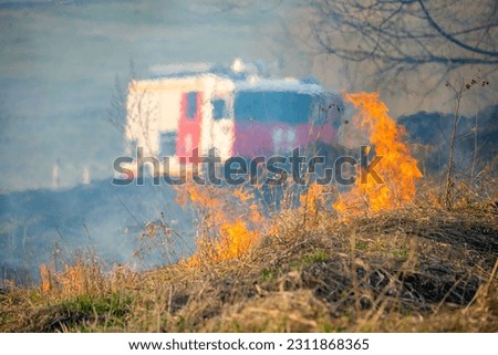 Burning dry grass in a field with a fire truck in the background.