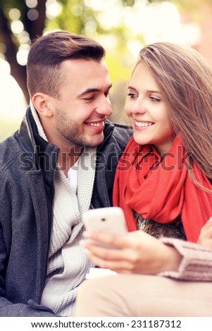 A picture of a young couple on a bench with smartphone in the park