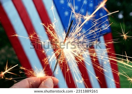 Holding a sparkler in front of an American Flag to celebrate the 4th of July Independence Day Royalty-Free Stock Photo #2311889261