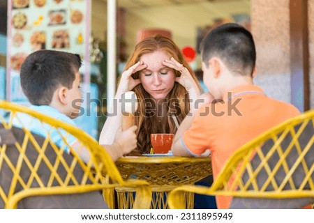 Stressed mother on a terrace of a coffee shop with her two children Royalty-Free Stock Photo #2311895949