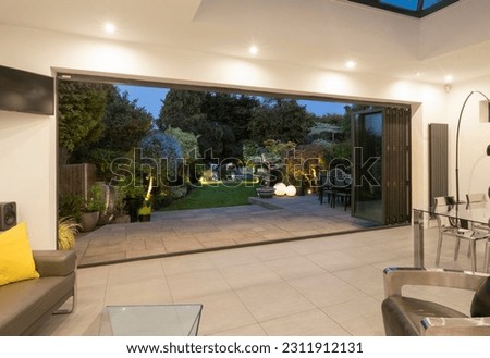 View through open bifold doors of attractive garden on a summer evening with lighting. Royalty-Free Stock Photo #2311912131