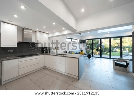 Interior of modern, white and grey designer open plan kitchen, with bifold doors and beautiful garden. Royalty-Free Stock Photo #2311912133
