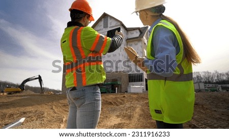 Wide angle view of woman project manager watching construction job foreman taking photos with tablet computer.