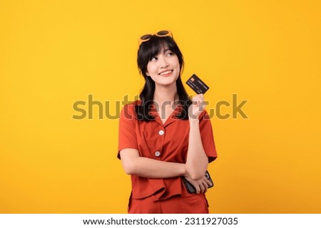 Portrait beautiful young asian woman happy smile dressed in orange clothes showing credit card isolated on yellow background. Pay and purchase shopping payment concept.