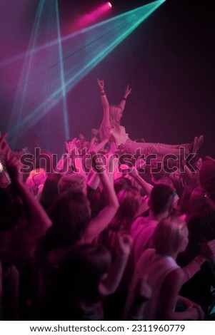 Crowd surf, neon and people at music festival with neon pink lighting and energy at live concert event. Dance, fun and group of excited gen z fans in arena at rock band performance or audience party.