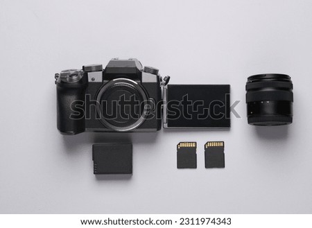 Modern digital camera with flip screen, two sd memory cards, battery and lens on gray background. Photographer's equipment. Top view. Flat lay