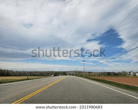 An open rural highway under a cloudy morning sky running through farm land.