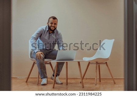 A confident businessman sitting and using laptop with a determined expression, while a beige background enhances the professional atmosphere, showcasing his productivity and expertise.