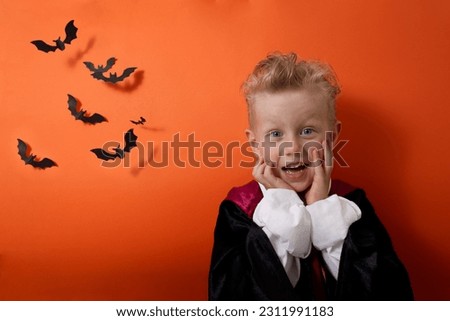 A boy in a vampire costume emotionally looks at the camera on an orange background